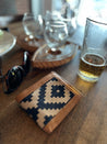 Close-up of a wooden table featuring the Zilker Belts Bogey Wallet with Argentine woven fabric, sunglasses, empty glasses, a half-full glass of beer, and a wooden serving tray.