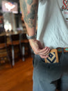 A person with a tattooed arm and watch puts a Zilker Belts Bogey Wallet into the back pocket of black jeans.