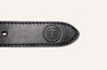 Close-up of the end of a black Argentine suede leather strap from Zilker Belts' Texas Exes II collection, featuring visible stitching and an embossed circular logo containing the letters 'ETX.'