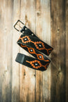 The Texas Exes II by Zilker Belts, featuring intricate orange geometric patterns on black, is coiled against a wooden background.