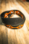 A close-up of a Texas Exes II belt by Zilker Belts, featuring a geometric orange and black pattern, crafted from black Argentine suede leather, lying on a wooden surface.